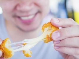 Man is going to eat sticky stretch fried cheese ball. Photo is focused at cheese ball