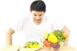 hombre asiático que muestra disgusto por la expresión de verduras frescas y coloridas aisladas sobre fondo blanco foto