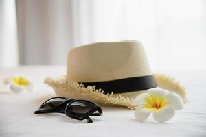 Tourist stuff hat sun glasses and plumeria flower in white bed room - happy relax vacation holiday and hotel concept photo