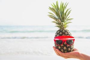 Encantadora piña fresca poniendo vasos en manos de turistas con fondo de olas marinas - diversión feliz con concepto de vacaciones saludables foto