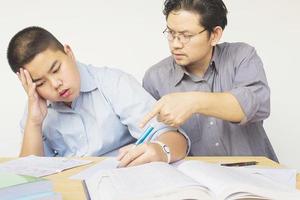 padre asiático enseñando la tarea a su hijo de 14 años en serio foto