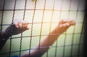 Dark portrait of a boy and holding steel screen or chain link fence - stressed sad child with no freedom concept photo