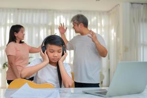 Asian boy kid wearing headphones and play loud music. so as not to hear quarrel while parents having fight or quarrel conflict at home. Unhappy problem in family, Domestic problems in the family. photo