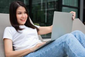 feliz joven empresaria sentada en una cama de bronceado junto a la piscina y usando una computadora portátil para trabajar en línea a distancia digital, proyecto de negocios en línea en un patio tranquilo de una casa de vacaciones, trabajar de vacaciones foto