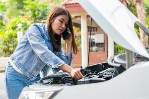 Angry Asian woman and using mobile phone calling for assistance after a car breakdown on street. Concept of vehicle engine problem or accident and emergency help from Professional mechanic photo