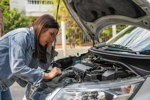 mujer asiática enojada y usando un teléfono móvil pidiendo ayuda después de una avería en el coche en la calle. concepto de problema del motor del vehículo o accidente y ayuda de emergencia de un mecánico profesional foto