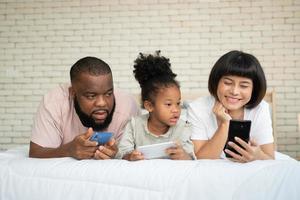 The family has fun and plays education games online with a smartphone at home in the bedroom. Concept of online education and caring from parents. photo