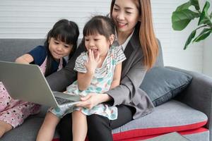 madre asiática con sus dos nietos divirtiéndose y jugando juegos educativos en línea con una computadora portátil digital en casa en la sala de estar. concepto de educación en línea y cuidado de los padres. foto