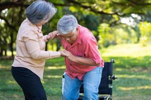 un anciano asiático se cayó en el suelo del parque después de tropezar y llorar de dolor y su esposa vino a ayudar. concepto de seguro de ancianos y atención médica foto