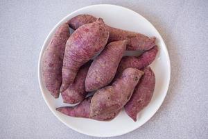 Close-up of fresh purple yams pile on white dish with gray background photo