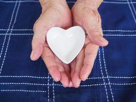 primer plano vista parcial del corazón de cerámica blanca en manos de mujer mayor foto