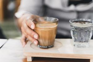 la mujer sostiene un vaso de espresso sobre leche fresca fría. café sucio, menú de café, café con leche foto