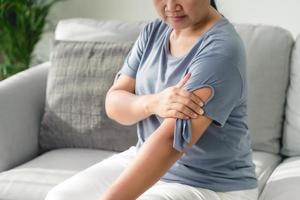 dolor de brazos. mujer que sufre de sensación de dolor en los músculos del brazo sentada en el sofá. concepto sanitario y médico. foto