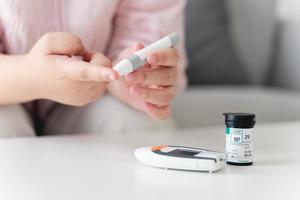 Mujer asiática con lanceta en el dedo para controlar el nivel de azúcar en la sangre con un medidor de glucosa, atención médica y médica, diabetes, concepto de glucemia foto