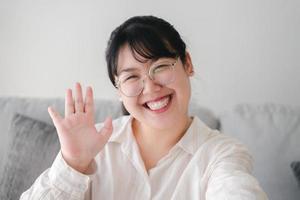 joven asiática que usa un teléfono inteligente para una videoconferencia en línea con amigos saludando con la mano haciendo un gesto de saludo foto