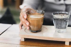 la mujer sostiene un vaso de espresso sobre leche fresca fría. café sucio, menú de café, café con leche foto