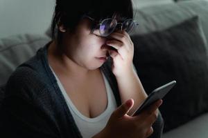 stressed woman take off glasses massage eyes feel fatigue suffering from headache, exhausted woman having eyestrain using smartphone in dark living room at night. photo