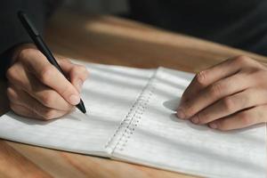 Close up of young man in casual cloth hands writing down on the notepad, notebook using ballpoint pen on the table. photo