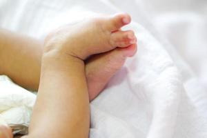 Tiny baby feet or new born baby feet on cozy white blanket with legs or feet crossed. photo