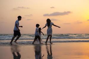 silueta familia caminando y jugando al atardecer en la playa con niños felices vacaciones concepto foto