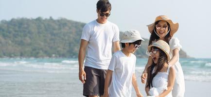 familia asiática caminando en la playa con niños felices vacaciones concepto foto