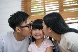 Happy young asian father and mother are kissing her daughter's cheek photo