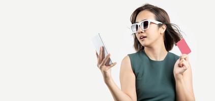 joven asiática con anteojos comprando por teléfono y con tarjeta para pago. disfrute del concepto de pago con tarjeta de crédito de la tienda feliz foto