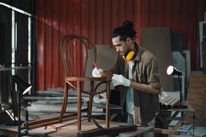 joven carpintero asiático que trabaja en un taller de carpintería de madera. foto