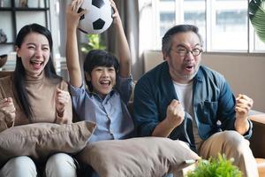 familia asiática viendo partidos de fútbol en la televisión y reaccionando feliz saliendo cuando el equipo dispara la pelota al gol. foto