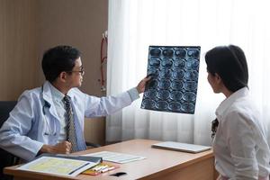 Asian doctor holding x-ray radiography to patient reviewing brain X-ray. photo