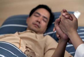 sosteniendo la mano paciente hombre asiático en el hospital. foto