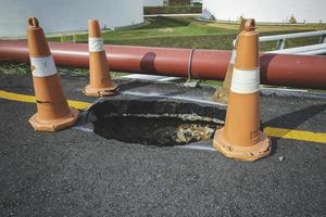 sumidero profundo en una ciudad callejera y cono de tráfico naranja. agujero peligroso en la carretera de asfalto foto