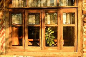 Windows of an old traditional village house with wooden frames, timbered and red bricked, in bright golden sunlight of evening hours, exterior closeup photo