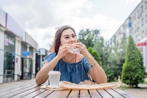 Stylish millennial woman eating burger at street cafe in summer photo