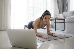 entrenamiento en casa una chica deportiva hace ejercicio en una colchoneta de yoga en posición negra para el cuerpo central y el abdomen mientras ve un tutorial en línea a través de una computadora portátil con un entrenador personal. foto