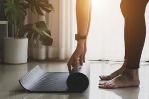 mujer joven con ropa deportiva negra practicando yoga y meditando en la sala de estar. hermosa chica preparando material para la clase de práctica. tranquilidad y relajación. felicidad femenina y concepto de yoga. foto