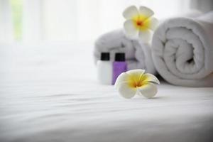 Hotel towel and shampoo and soap bath bottle set on white bed with plumeria flower decorated - relax vacation at the hotel resort concept photo