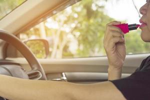 Woman making up her face using lipstick while driving car, unsafe behavior photo