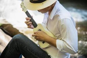 Man play ukulele new to the river- people and music instrument life style in nature concept photo