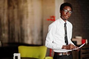 Business african american man wear on white shirt, tie and glasses at office, holding papers on hand and write something. photo