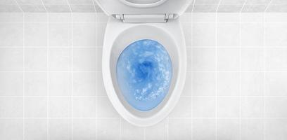 Top view of toilet bowl, blue detergent flushing in it photo