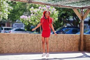 Cute and slim african american girl in red dress with dreadlocks in motion having fun on street. Stylish black model. photo