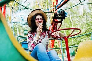 Portrait of brunette girl in pink glasses and hat with ice cream at amusement park. photo