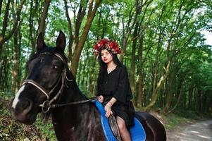 Mystical girl in wreath wear in black at horse in wood. photo