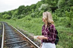 Portrait of a pretty blond girl in tartan shirt walking on the railway with map in her hands. photo