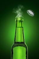 botella de cerveza fría y húmeda abierta con humo sobre fondo verde foto