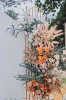 arreglo floral para la boda de verano, hecho de rosas y ramas verdes en una mesa en el restaurante. , vidrio y platos en el restaurante al aire libre en un día ventoso con efecto de grano de película foto