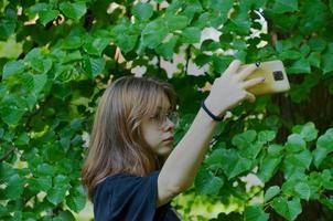 a girl takes pictures of herself on her phone near the trees photo