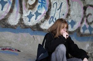 St. Petersburg, Russia, 06.01.2022. A teenage girl sits in an abandoned building painted with graffiti and smokes photo