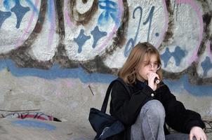 St. Petersburg, Russia, 06.01.2022. A teenage girl sits in an abandoned building painted with graffiti and smokes photo